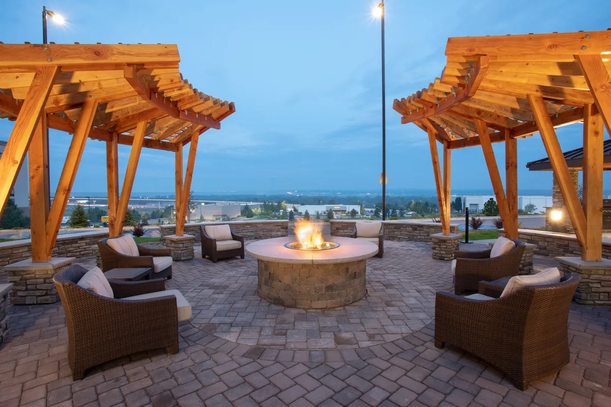 This image captures the hotel's exterior communal area featuring a fire pit, wooden pergolas, and a spacious seating area. Guests are seen gathering around the fire, creating a lively and inviting atmosphere suited for relaxation and informal socializing after a day of business meetings or travel.