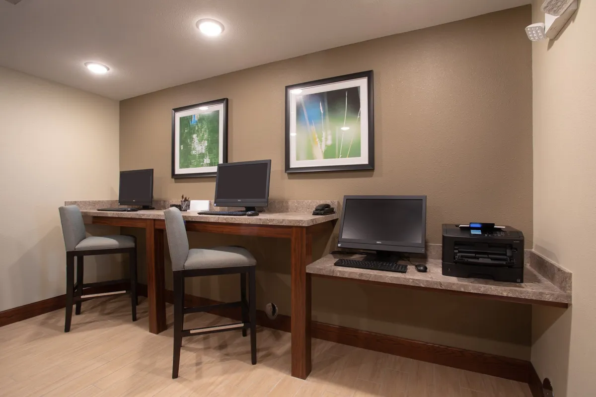 This image features a dedicated work area with desks, computers, and a printer. The scene highlights a welcoming, communal workspace decorated with colorful artwork, suggesting a comfortable environment for productivity. There are signs of quiet activity, with people focusing on computers and collaborating.