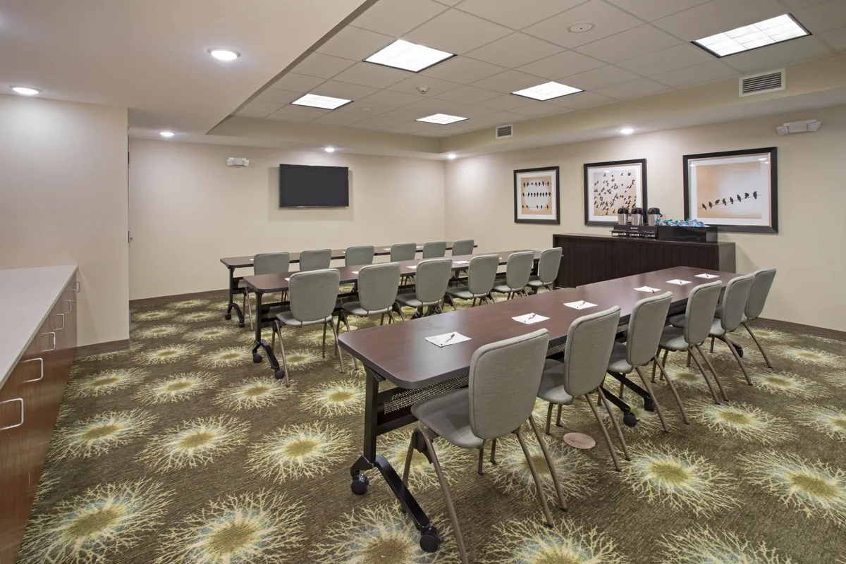 A spacious conference room with a long table, modern chairs, vibrant wall art, and a television screen set up for meetings or group gatherings. The layout encourages group activities, planning sessions, or socializing with family or colleagues.