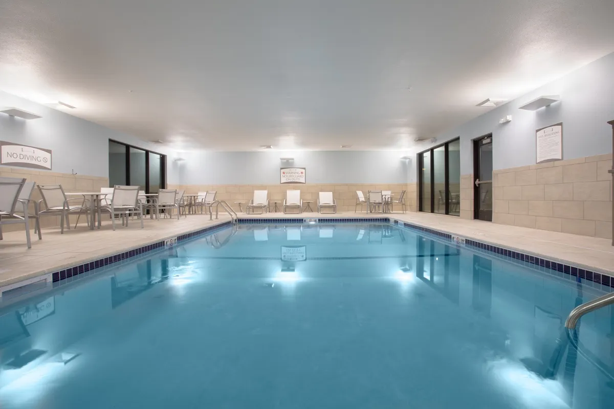 An inviting indoor swimming pool with sparkling water, comfortable lounge chairs, and soft pool lights creating a tranquil ambiance. Guests are shown swimming and relaxing, taking advantage of exclusive pool access.