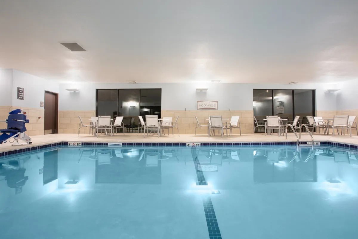 An interior pool area bathed in natural light from large windows, featuring lounge chairs and soft lighting fixtures. The scene conveys tranquility, offering a glimpse of a space ideal for unwinding, relaxing with a book, or enjoying a peaceful swim.