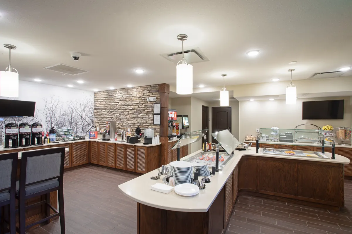 A welcoming breakfast area with a prominent food display, coffee station, and comfortable seating. The stone wall and modern decor create an inviting atmosphere, ideal for starting the day with a fresh coffee or complimentary buffet breakfast.