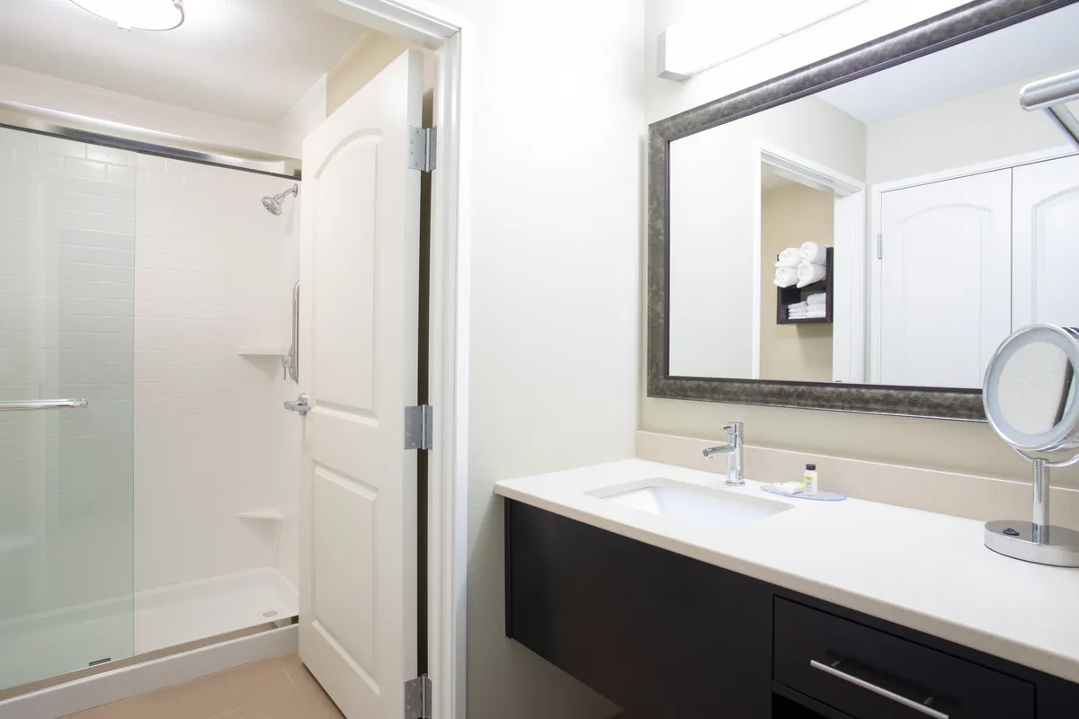 A modern bathroom featuring a glass-door shower, a sleek vanity with a large mirror, and towels neatly arranged. The space is filled with natural light and appears impeccably clean and inviting, with visible toiletries and cozy bath linens.